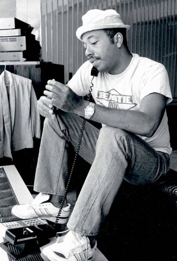 Movie still from “Beastie Boys Story” (2020), directed by Spike Jonze – A black and white photo of a man sitting on the floor holding a phone; Medium shot, Low angle