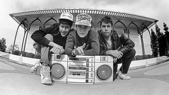 Movie still from “Beastie Boys Story” (2020), directed by Spike Jonze – A group of young men sitting next to each other on top of a radio; Medium shot, Low angle