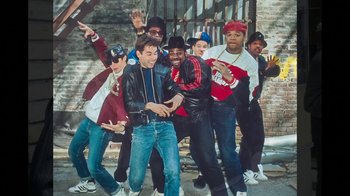 Movie still from “Beastie Boys Story” (2020), directed by Spike Jonze – A group of young men standing next to each other in front of a brick wall; Medium shot, Overhead angle