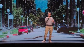 Movie still from “Beastie Boys Story” (2020), directed by Spike Jonze – A man standing in front of a screen with cars on it; Wide shot, High angle