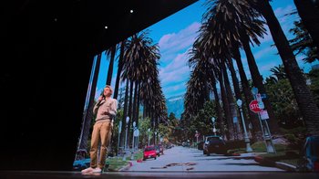 Movie still from “Beastie Boys Story” (2020), directed by Spike Jonze – A man standing in front of a large screen with palm trees in front of him; Wide shot, Low angle