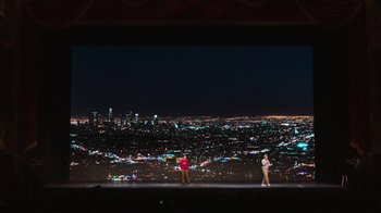 Movie still from “Beastie Boys Story” (2020), directed by Spike Jonze – Two people are standing on a stage in front of a city skyline at night; Extreme Wide shot, Low angle