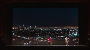 Movie still from “Beastie Boys Story” (2020), directed by Spike Jonze – Two people standing on a stage in front of a city skyline at night; Extreme Wide shot, Low angle