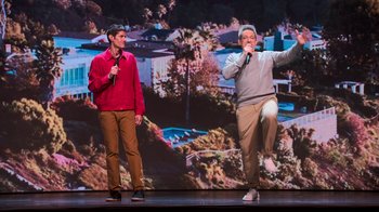 Movie still from “Beastie Boys Story” (2020), directed by Spike Jonze – Two men stand on a stage and one man holds a microphone while the other sings; Wide shot, Low angle