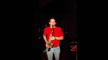 Movie still from “Beastie Boys Story” (2020), directed by Spike Jonze – A man holding a saxophone in a room; Medium shot, Low angle