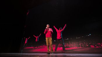 Movie still from “Beastie Boys Story” (2020), directed by Spike Jonze – A man standing on a stage while holding a microphone to his mouth; Wide shot, Low angle