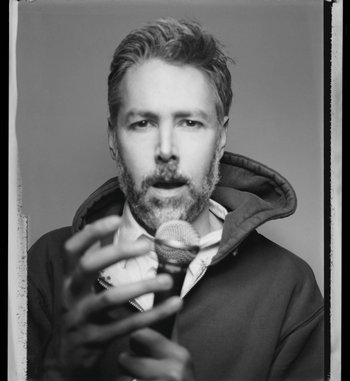 Movie still from “Beastie Boys Story” (2020), directed by Spike Jonze – A black and white photo of a man holding a glass; Close Up shot, Overhead angle