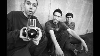 Movie still from “Beastie Boys Story” (2020), directed by Spike Jonze – Three young men sitting on the ground holding a camera; Medium shot, Low angle