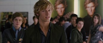 A young man with blonde curly hair wearing a black suit