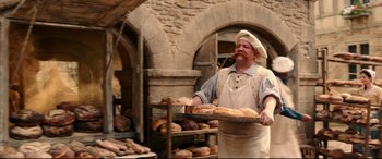 Movie still from “Beauty and the Beast” (2017), directed by Bill Condon – A man holding a tray of bread in a bakery; Medium shot, Over the shoulder angle