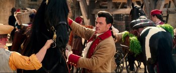 Movie still from “Beauty and the Beast” (2017), directed by Bill Condon – A man in a red and brown jacket is tying a horse's bridle; Medium shot, Over the shoulder angle