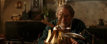 Movie still from “Beauty and the Beast” (2017), directed by Bill Condon – An older man holding a wooden cross in his hands; Medium shot, Over the shoulder angle