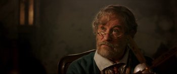 Movie still from “Beauty and the Beast” (2017), directed by Bill Condon – An old man with a beard and glasses sitting in a chair; Close Up shot, Over the shoulder angle