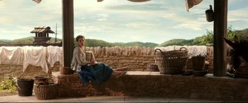 Movie still from “Beauty and the Beast” (2017), directed by Bill Condon – A woman sitting on a ledge holding an open book; Wide shot, High angle