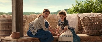 Movie still from “Beauty and the Beast” (2017), directed by Bill Condon – Two young women sitting next to each other on a stone wall; Medium shot, High angle