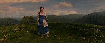 Movie still from “Beauty and the Beast” (2017), directed by Bill Condon – A woman standing in a field of grass with mountains in the background; Wide shot, Low angle