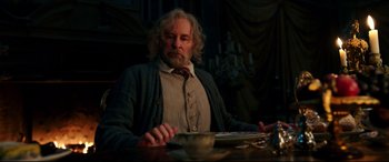Movie still from “Beauty and the Beast” (2017), directed by Bill Condon – An older man sitting at a table in a dark room; Medium shot, Low angle