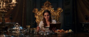 Movie still from “Beauty and the Beast” (2017), directed by Bill Condon – A beautiful young lady sitting at a dinner table; Medium shot, Low angle