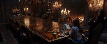 Movie still from “Beauty and the Beast” (2017), directed by Bill Condon – A woman sitting at a table in front of candles; Wide shot, High angle