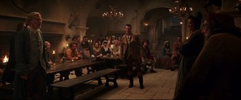 Movie still from “Beauty and the Beast” (2017), directed by Bill Condon – A man standing in front of a group of people; Wide shot, Over the shoulder angle