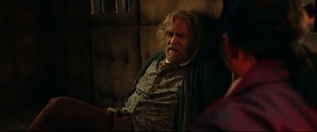 Movie still from “Beauty and the Beast” (2017), directed by Bill Condon – An older man sitting on a couch in a dark room; Medium shot, Over the shoulder angle