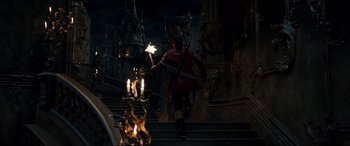 Movie still from “Beauty and the Beast” (2017), directed by Bill Condon – A man in a red robe holding a sword and a candle; Wide shot, High angle