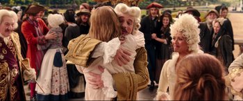 Movie still from “Beauty and the Beast” (2017), directed by Bill Condon – Two people in period costumes hug in front of a group of onlookers; Medium shot, Over the shoulder angle
