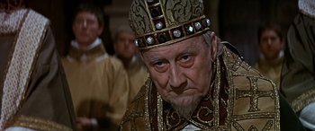 Movie still from “Becket” (1964), directed by Peter Glenville – An old man wearing a crown in a crowd of people; Close Up shot, Over the shoulder angle