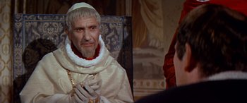 Movie still from “Becket” (1964), directed by Peter Glenville – An old man wearing a white robe and holding a cross; Close Up shot, Over the shoulder angle
