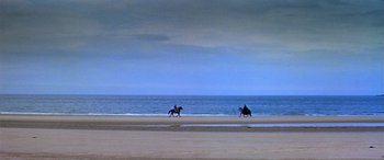 Movie still from “Becket” (1964), directed by Peter Glenville – Two people riding horses on the beach near the ocean; Extreme Wide shot, High angle