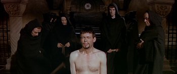 Movie still from “Becket” (1964), directed by Peter Glenville – A man with no shirt is standing in front of two other men; Medium shot, High angle