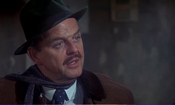 Movie still from “Bedknobs and Broomsticks” (1971), directed by Ward Kimball – An older man wearing a green hat and a tie; Close Up shot, Over the shoulder angle