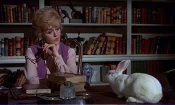 Movie still from “Bedknobs and Broomsticks” (1971), directed by Ward Kimball – A woman sitting at a table with a rabbit; Medium shot, High angle