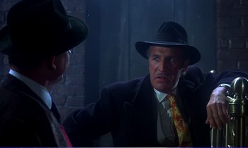 Movie still from “Bedknobs and Broomsticks” (1971), directed by Ward Kimball – A man wearing a suit and hat talking to another man; Medium shot, Over the shoulder angle