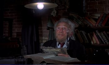 Movie still from “Bedknobs and Broomsticks” (1971), directed by Ward Kimball – An old man sitting at a table holding a book; Medium shot, Low angle