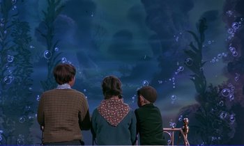 Movie still from “Bedknobs and Broomsticks” (1971), directed by Ward Kimball – Three children looking at a fish tank at night time; Wide shot, High angle