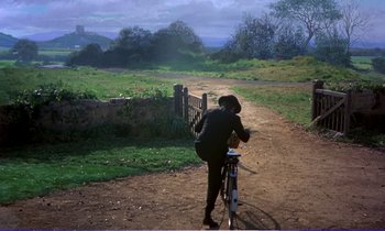 Movie still from “Bedknobs and Broomsticks” (1971), directed by Ward Kimball – A person riding a bike on a dirt road near a fence; Wide shot, High angle