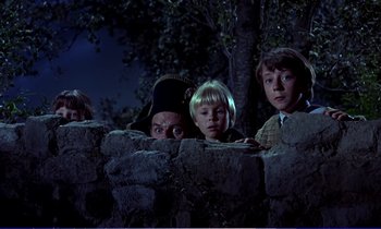 Movie still from “Bedknobs and Broomsticks” (1971), directed by Ward Kimball – A group of kids standing next to a stone wall at night; Medium shot, Low angle