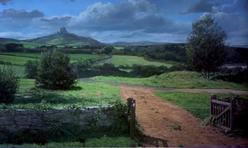 Movie still from “Bedknobs and Broomsticks” (1971), directed by Ward Kimball – A dirt road going through a field with a castle in the background; Extreme Wide shot, High angle
