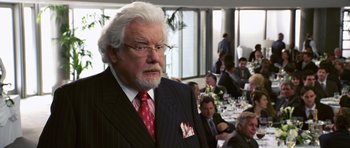 Movie still from “Bedtime Stories” (2008), directed by Adam Shankman – An older man in a suit and tie in front of a group of diners; Close Up shot, Over the shoulder angle