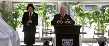 Movie still from “Bedtime Stories” (2008), directed by Adam Shankman – A man standing at a podium speaking to a crowd; Medium shot, Over the shoulder angle