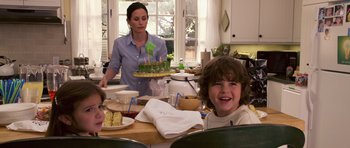 Movie still from “Bedtime Stories” (2008), directed by Adam Shankman – A woman and a child sitting at a table with a cake on it; Medium shot, Over the shoulder angle