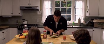 Movie still from “Bedtime Stories” (2008), directed by Adam Shankman – A man is cutting a sandwich on top of a plate; Medium shot, Over the shoulder angle