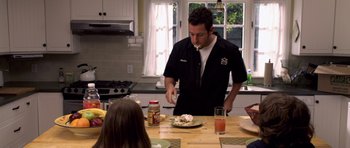 Movie still from “Bedtime Stories” (2008), directed by Adam Shankman – A man standing at a table with food in front of him; Medium shot, Over the shoulder angle