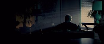 Movie still from “Bedtime Stories” (2008), directed by Adam Shankman – An older man sitting on a couch in a dark room; Wide shot, Low angle