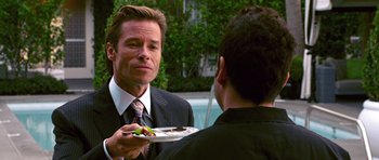 Movie still from “Bedtime Stories” (2008), directed by Adam Shankman – A man wearing a suit and tie holding a plate of food; Close Up shot, Over the shoulder angle