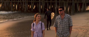 Movie still from “Bedtime Stories” (2008), directed by Adam Shankman – A man and a woman walking on the beach with surfboards; Medium shot, Over the shoulder angle