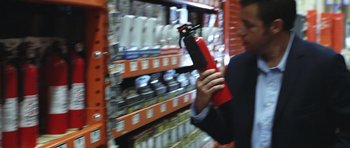 Movie still from “Bedtime Stories” (2008), directed by Adam Shankman – A man holding a red fire extinguisher in a store; Medium shot, Over the shoulder angle