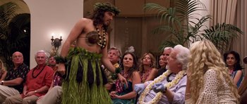 Movie still from “Bedtime Stories” (2008), directed by Adam Shankman – A group of people gathered around a man in a hula outfit; Medium shot, Over the shoulder angle