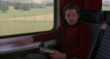 Movie still from “Before Sunrise” (1995), directed by Richard Linklater – A man sitting on a train holding a book; Medium shot, Over the shoulder angle